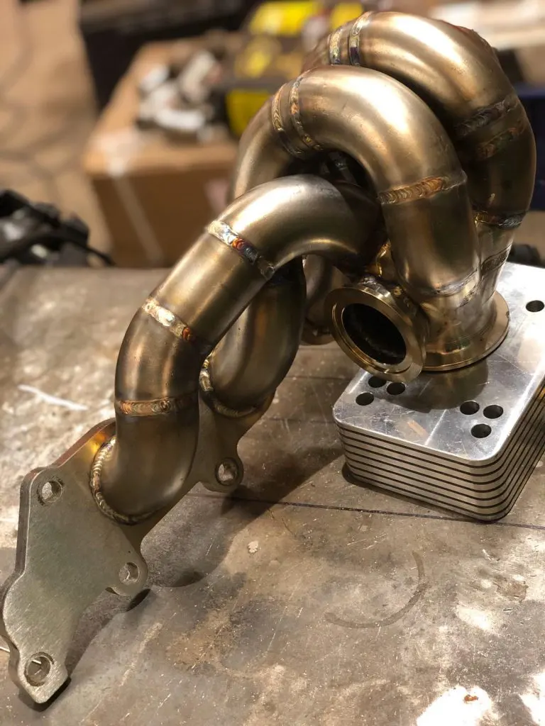 A finished four-into-one turbo manifold on the bench, heat tint still across the runners