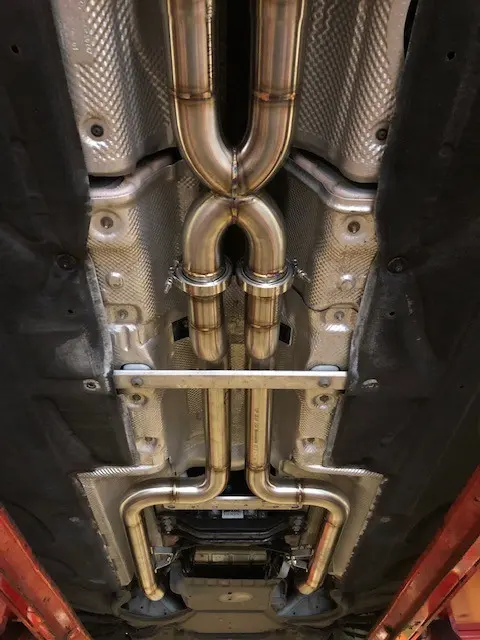 A finished stainless system fitted under a car on the ramp, twin pipes over the axle